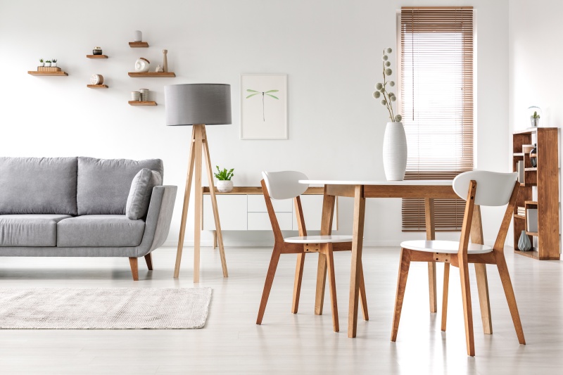 Wooden chairs at table in bright open space interior with lamp next to grey couch. Real photo Wooden chairs at table in bright open space interior with lamp next to grey couch. Real photo